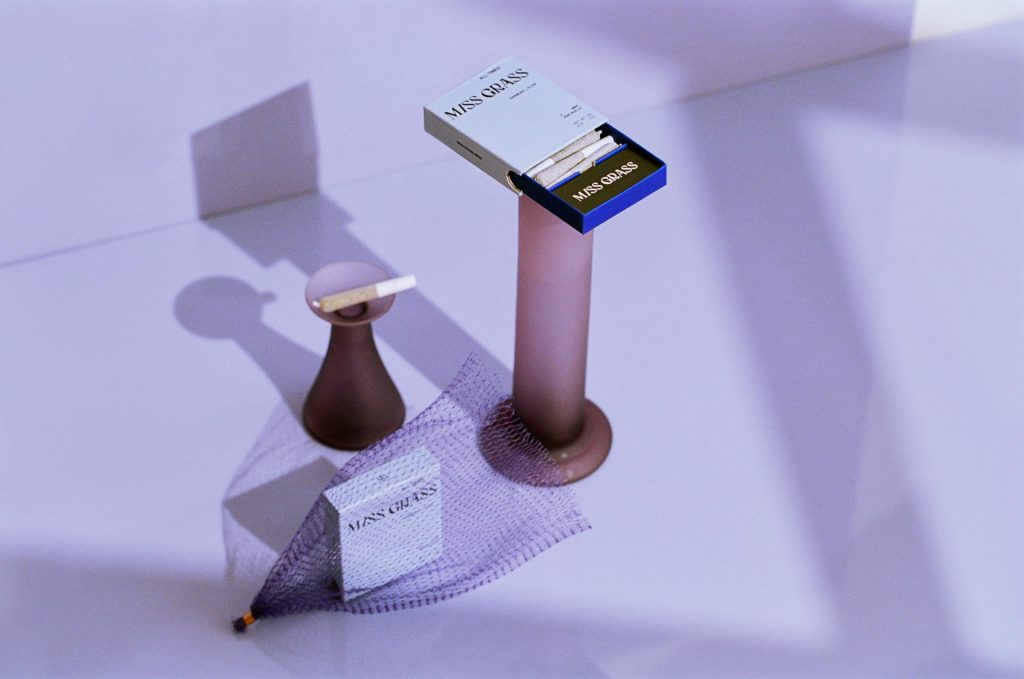 Shore House Canna Cape May dispensary product photo featuring Miss Grass mini pre-rolls in a blue and white pack, displayed in a minimalist lavender-toned setting with sculptural stands.